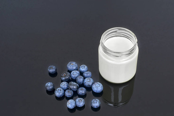 Frasco de vidro com iogurte e mirtilos em um fundo preto horizontal
 - Foto, Imagem