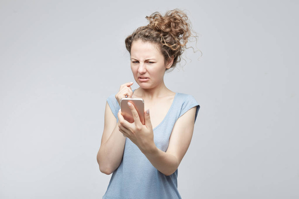 Closeup portrait anxious or shocked young freelancer woman looking at phone seeing bad news or photos with disgusting emotion on her face isolated grey background. Human emotion, reaction, expression. - Fotoğraf, Görsel