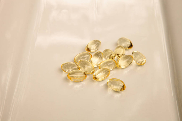 Χρυσό gel κάψα της βιταμίνης Ε, που εμφανίζεται σε μια λευκή επιφάνεια. - Φωτογραφία, εικόνα