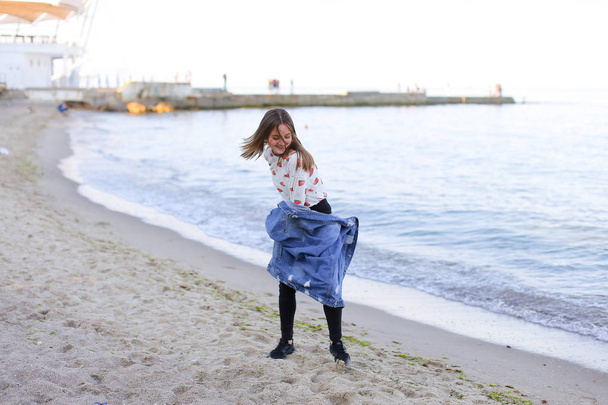Γοητευτικό κορίτσι περπατά κατά μήκος της ακτής και κουτσουκέλες χαρούμενα στην άμμο - Φωτογραφία, εικόνα