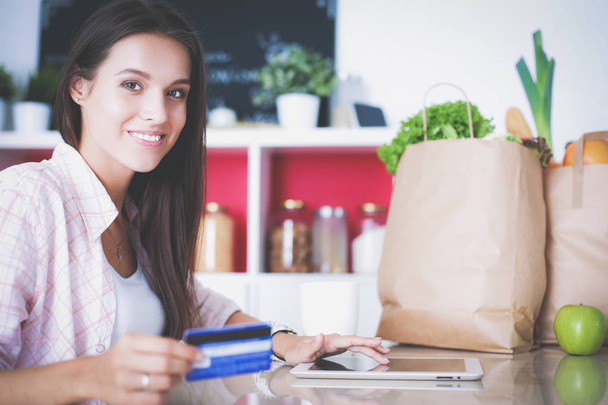 Smiling woman online shopping using tablet and credit card in kitchen - Foto, Imagem