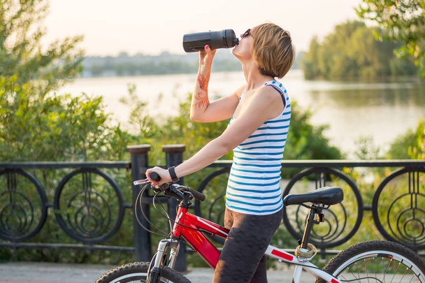 Femme monte un vélo et les boissons d'une bouteille de sport sur une allée
 - Photo, image