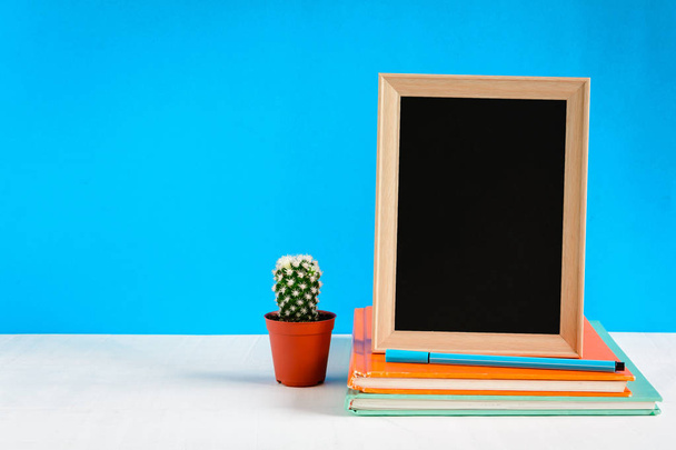 Μαυροπίνακας με χλεύη επάνω πλαίσιο και βιβλίο μολύβι πάνω στο ξύλινο τραπέζι - Φωτογραφία, εικόνα
