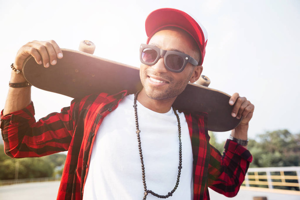 Young dark skinned man wearing sunglasses holding skateboard - Foto, Imagem