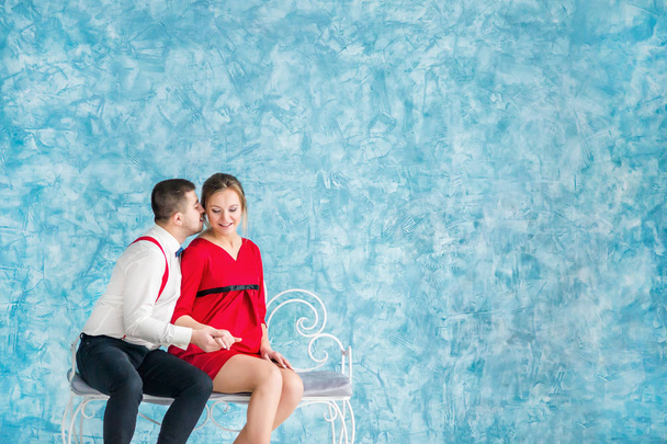 Liebendes junges Paar, das auf einer Bank sitzt, einander ansieht und sich auf einer Bank berührt. Mann und Frau sitzen auf einer Bank. Studioaufnahmen - Foto, Bild