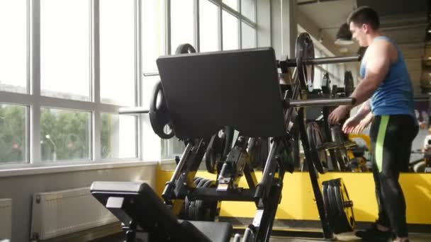 Gespierde sportieve man gewicht voor squats mashine toe te voegen in de sportschool - Video