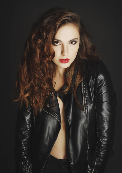 Beautiful young woman posing in black leather jacket over grey b - Foto, Imagen