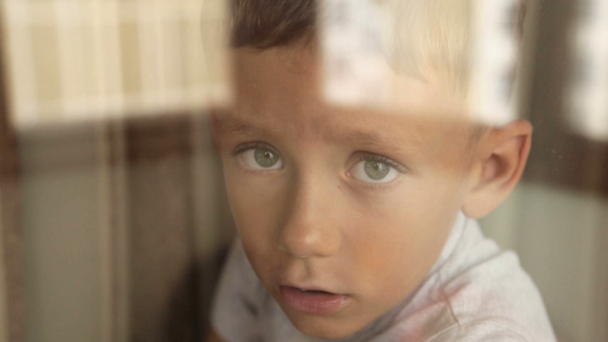 Een verdrietig kind kijkt uit het raam - Video