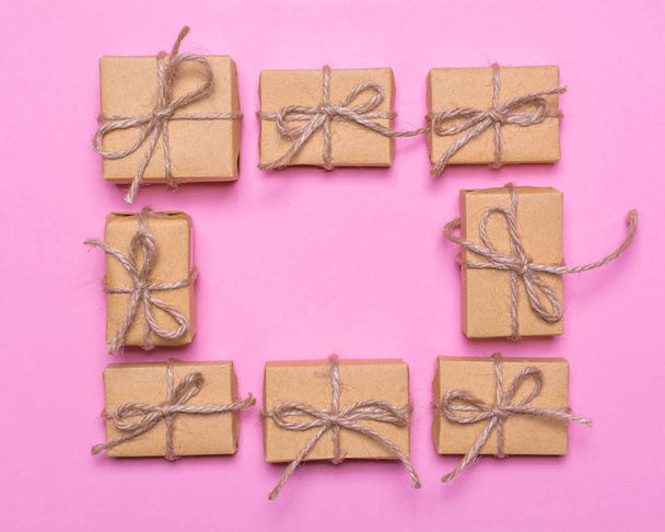 Una cornice di scatole regalo avvolto in carta kraft su uno sfondo rosa. design piatto lay, vista dall'alto
 - Foto, immagini