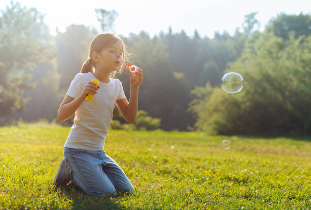 Little girl blowing bubbles in the meadow - Фото, изображение