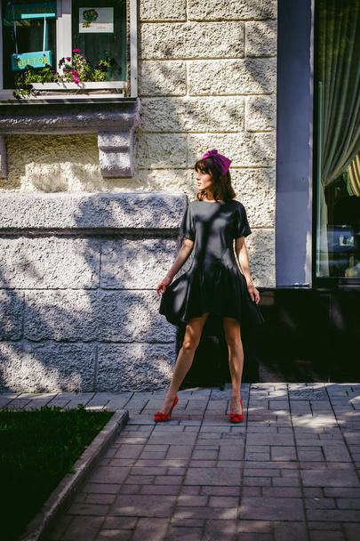 Krásná žena v tmavé stylové šaty procházky podél ulice, blízko butiků. Portrét módní dívky - Fotografie, Obrázek