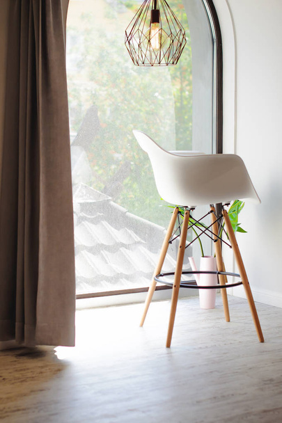 Fashionable white chair with wooden legs near the window - 写真・画像