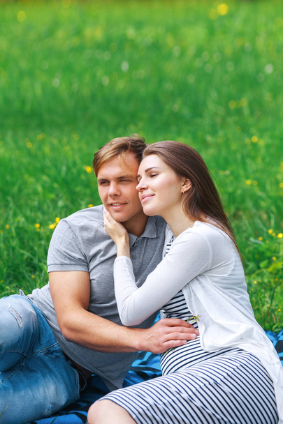 glückliche schwangere Frau mit ihrem Mann, der sich im Park umarmt und lächelt - Foto, Bild
