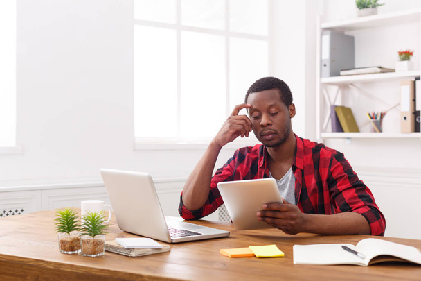 Серьезный молодой черный счастливый бизнесмен в офисе, работа с ноутбуком
 - Фото, изображение