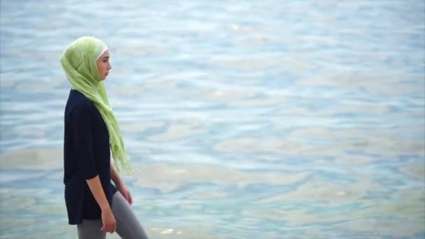 Uma jovem muçulmana de véu vem com um olhar pensativo ao longo do mar
 - Filmagem, Vídeo
