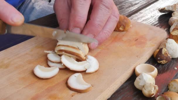Nice wild mushrooms are cut with knife into small pieces on wooden chopping board. Man hands cut boletus slice on wooden table  - Footage, Video