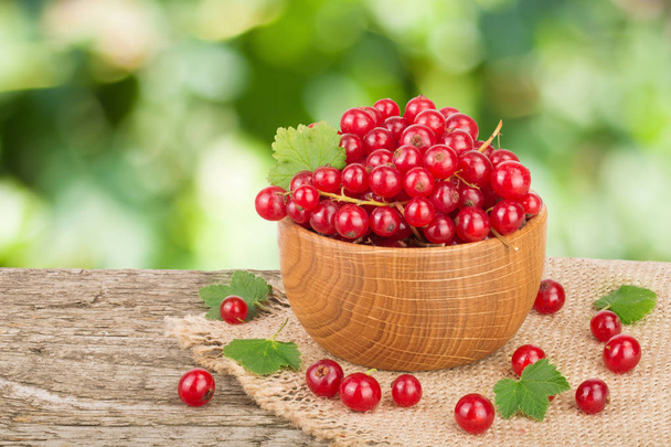 Red currant berries in wooden bowl on wooden table with blurry garden background - Foto, immagini