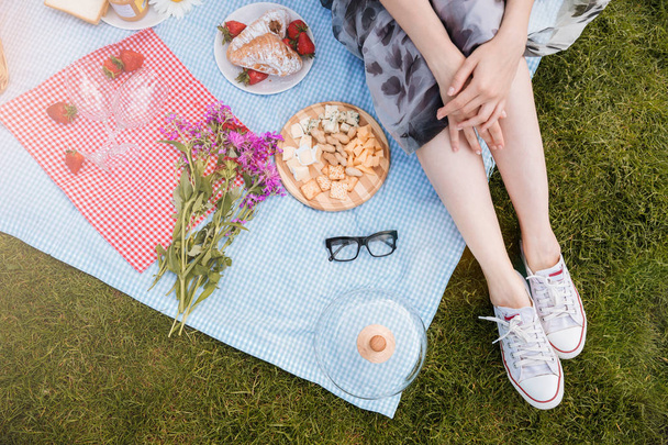 Legs of young woman sitting on blanket and having picnic - Foto, Imagen