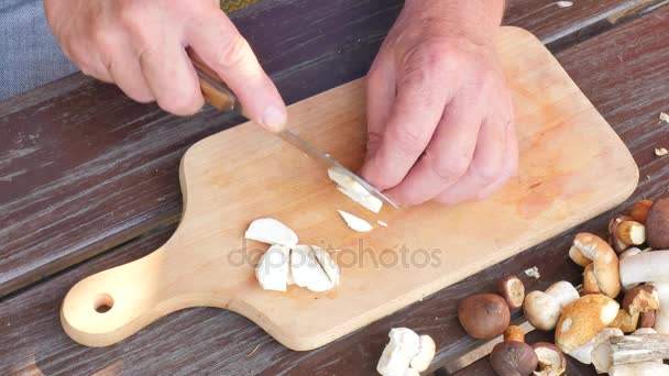 Рубите свежие дикие грибы. Крупным планом руки с ножом режут грибы. Мужская рука аккуратно режет дикие грибы на кухонной доске
  - Кадры, видео