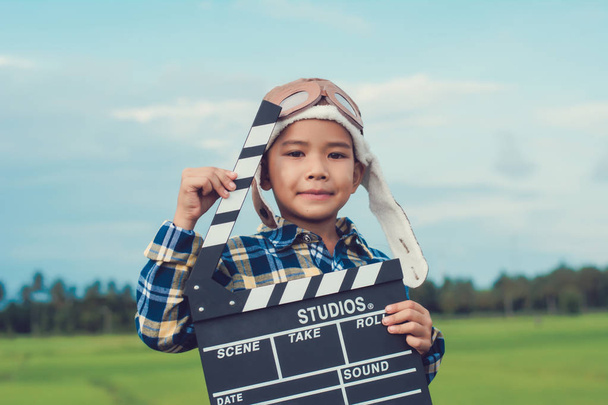 Kind spielt Filmklappbrett vor Sommerhimmel Hintergrund. Konzept des Regisseurs. - Foto, Bild