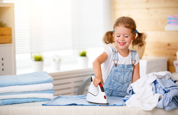 Happy   child girl ironing clothes   in laundry   - Foto, afbeelding