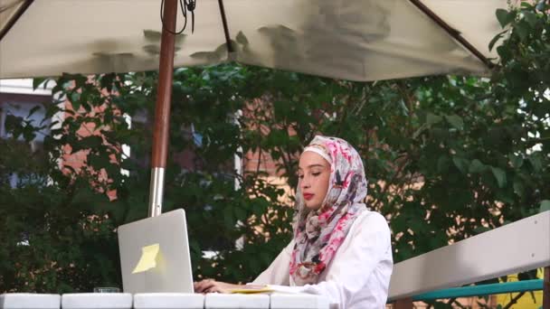Muzułmanka w hidżab drukuje wiadomość na laptopie, jest poza na wolnym powietrzu - Materiał filmowy, wideo