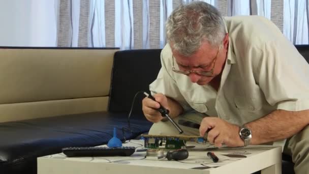 Man soldering a board with a soldering iron, he has in his hands a large magnifying glass - Filmati, video