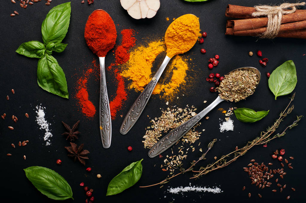 Spoons with spices and seasonings (turmeric, oregano, paprika) on dark ground. Next to other herbs and condiments - Fotoğraf, Görsel