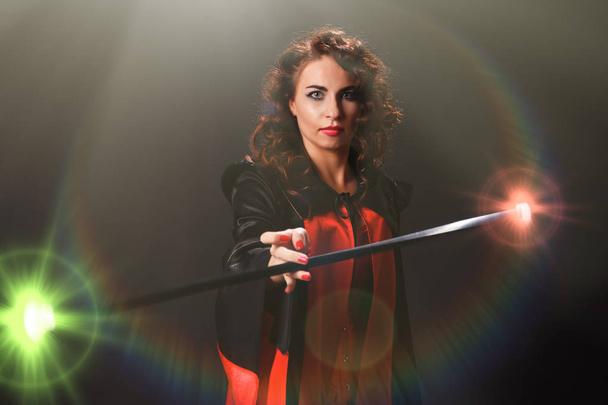 Belle femme à l'image d'une sorcière tourne dans ses mains un bâton magique qui émet des éclairs de couleurs vives
 - Photo, image