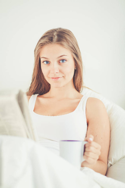 A pretty young woman reading the newspaper in bed and enjoying a cup of tea. - Photo, image