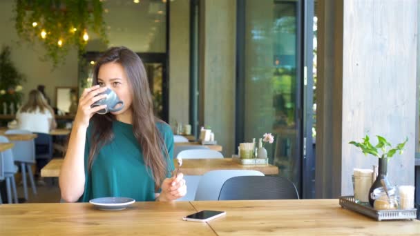 Young woman calling with cell telephone while sitting alone in coffee shop during free time. Attractive female with cute smile having talking conversation with mobile phone while rest in cafe - Footage, Video