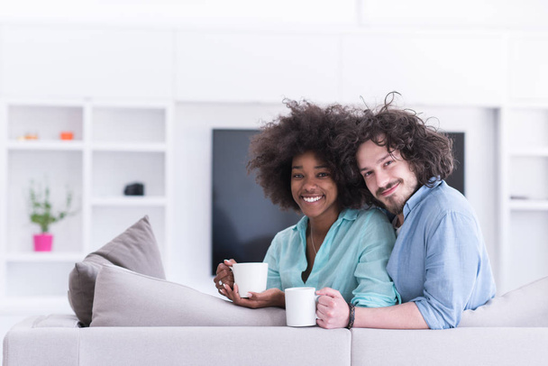 multiethnic couple sitting on sofa at home drinking coffe - Photo, image