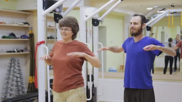 Νεαρός άνδρας και ηλικιωμένη γυναίκα απλώνεται, κάνει ασκήσεις στο γυμναστήριο. Υγιή γυμναστική. Δραστήρια άτομα. - Πλάνα, βίντεο