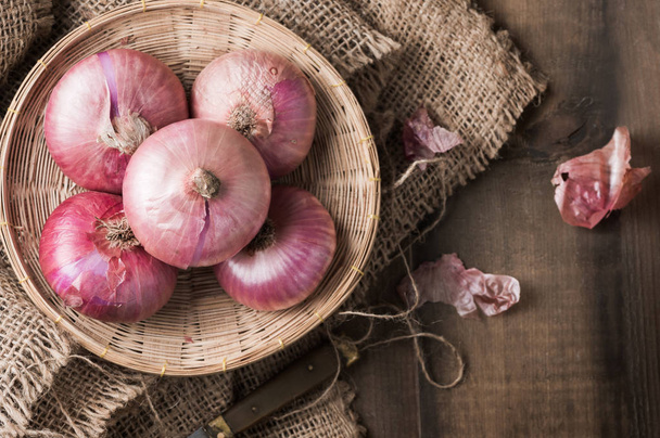 red onions in bamboo basket and on wood background. - Photo, Image