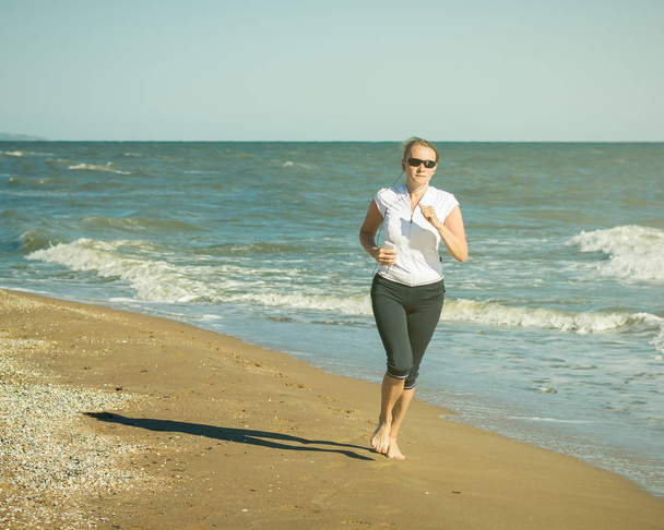 Μια γυναίκα εκτελεί μια άσκηση για το Berg τη θάλασσα στις ακτίνες του ήλιου. Ήπια. - Φωτογραφία, εικόνα