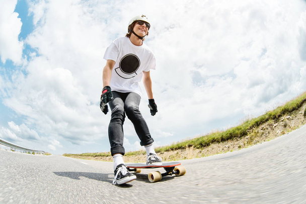 The young Longboarder pushes his foot out on his longboard over the country road - Zdjęcie, obraz