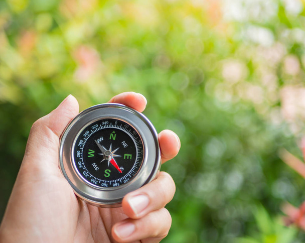 Closeup hand holding compass with  tree leaves bokeh  background - Photo, Image