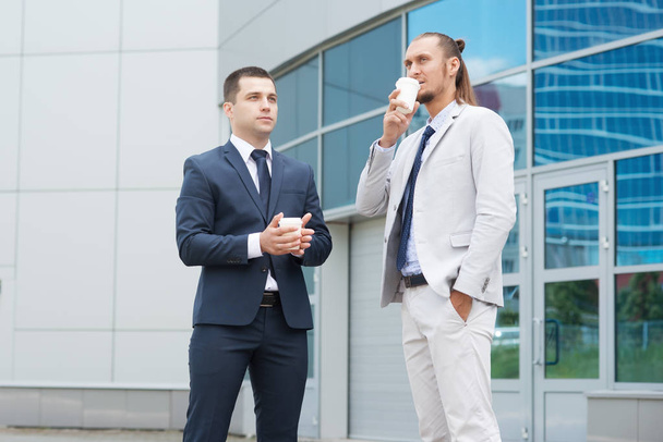 Двое бизнесменов задумчиво смотрят вдаль, размышляя на фоне бизнес-центра
 - Фото, изображение