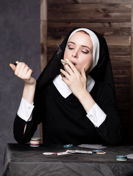 beautiful catholic nun smokes and playing cards. Rotten religion - Photo, Image