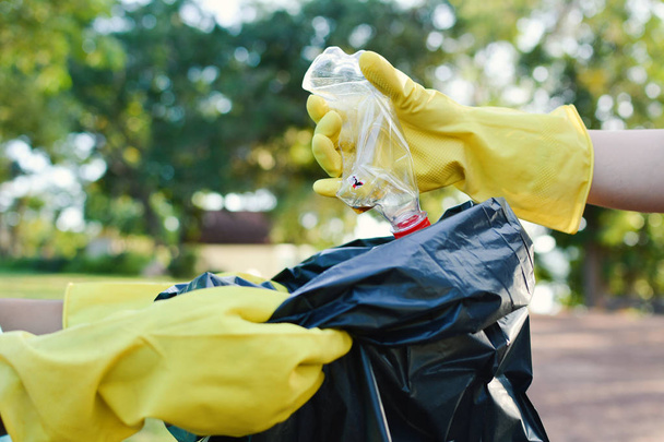 Hände in gelben Handschuhen heben leere Flaschen Plastik in Müllsack auf - Foto, Bild