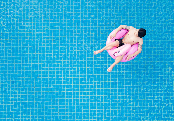Top view, a man relaxing on pink flamingo swimming pool float, on swimming pool in summer
 - Фото, изображение