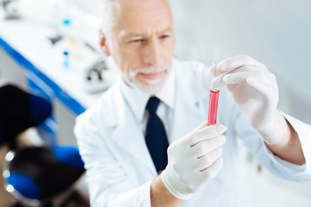 Concentrated elderly man examining pink liquid - Photo, Image