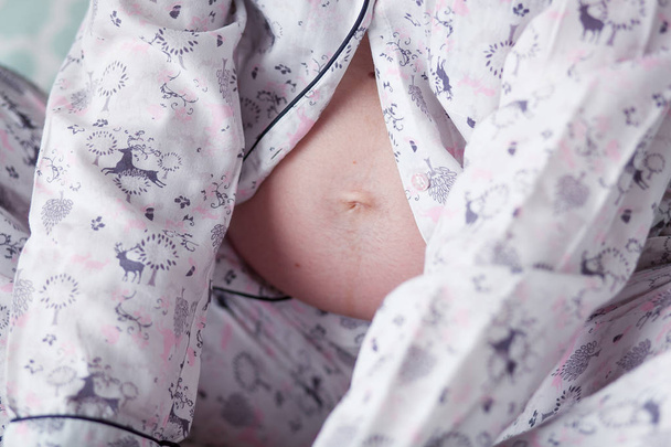 Κοντινό πλάνο εικόνα του μια κοιλιά της εγκύου στο πιτζάμες - Φωτογραφία, εικόνα