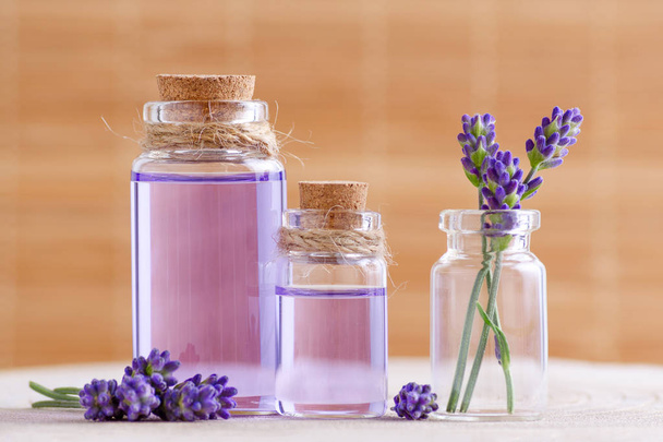 lavendel water en olie in glazen flessen en verse lavendel op stomp en bruine achtergrond - Foto, afbeelding
