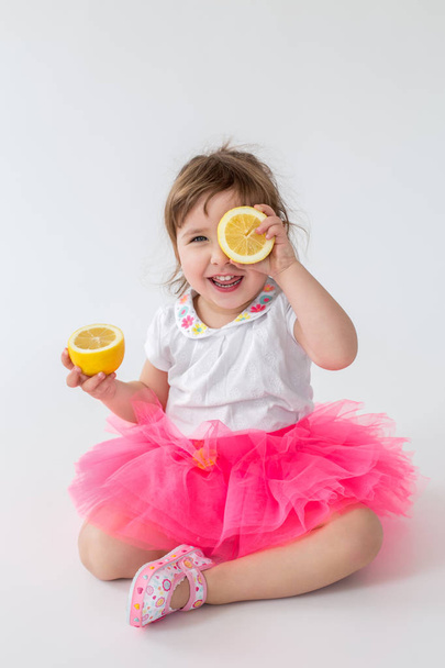 Happy little girl sitting while holding orange - Photo, Image