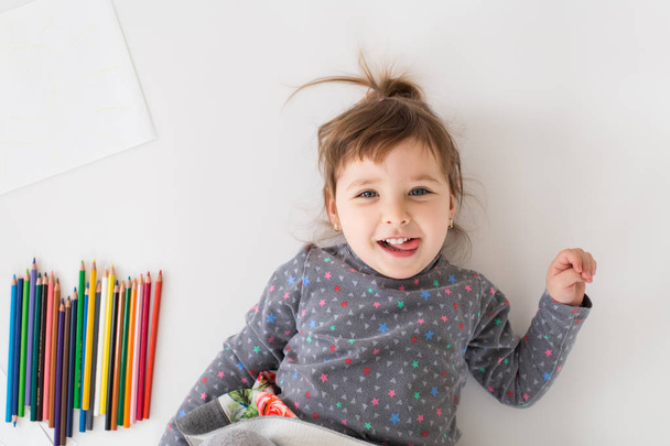 Cheerful little girl lies near a lot of colouring pencils - Photo, Image