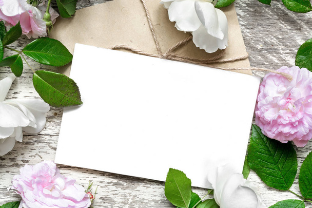 κενή άσπρη ευχετήρια κάρτα και φάκελο στο πλαίσιο της τριαντάφυλλα λουλούδια - Φωτογραφία, εικόνα