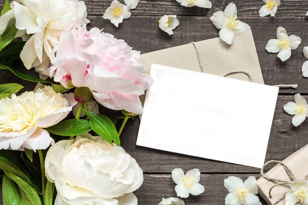 üres üdvözlőlap és boríték keretben, rózsaszín és fehér pünkösdi rózsa és jázmin virágok - Fotó, kép