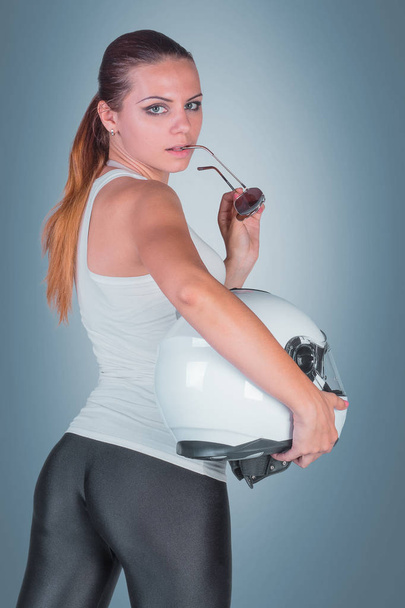 Beautiful young woman with moto helmet in studio on blue backgro - Фото, изображение