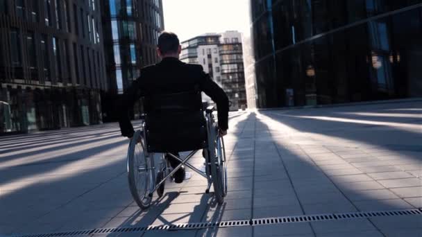 Achteraanzicht van een ongeldige zakenman in rolstoel wordt verplaatst in de zakenwijk. - Video
